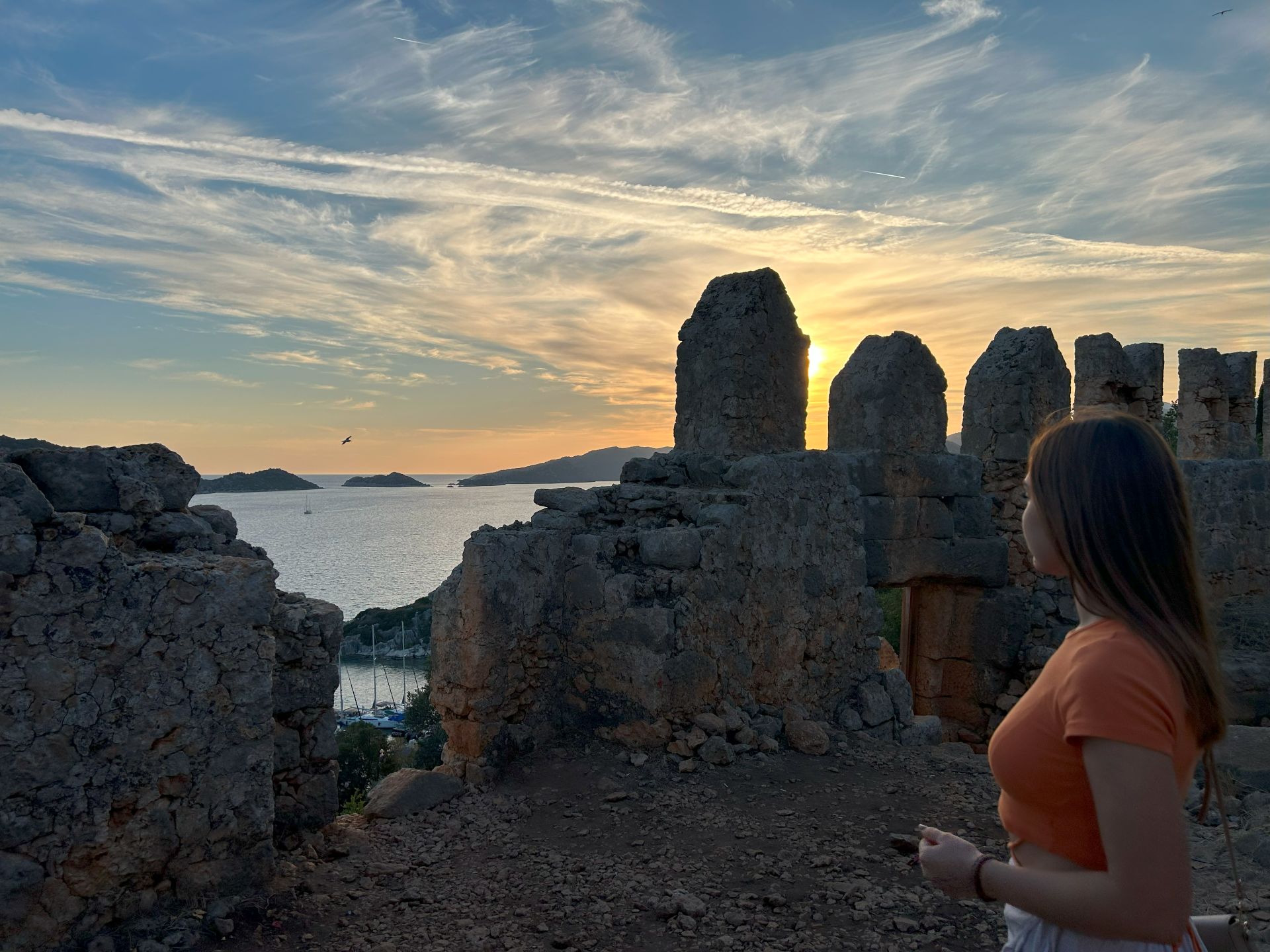 A panoramic view of Simena Castle perched atop Kaleköy, overlooking the turquoise waters of the Mediterranean, surrounded by lush landscapes and ancient ruins