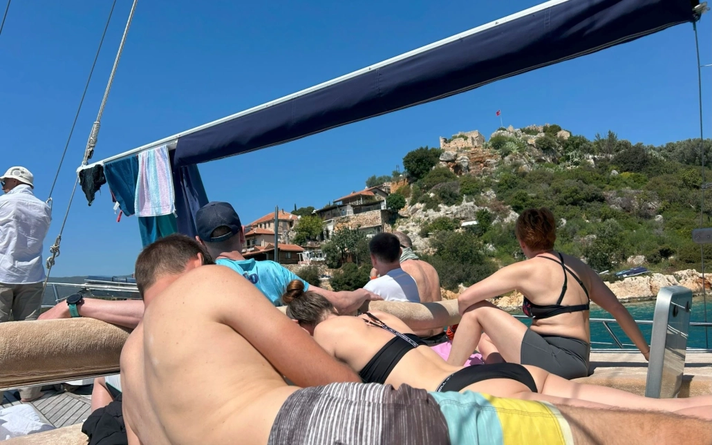 Group of people relaxing on the deck of a boat with a scenic view of Kalekoy Castle and traditional stone houses in Kekova.