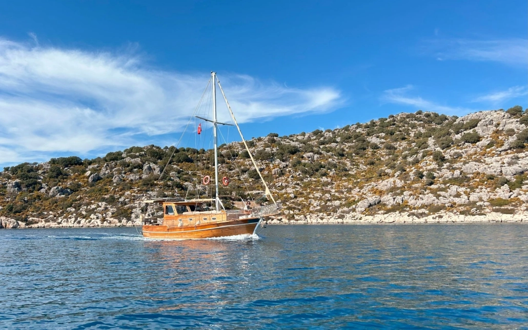 A traditional wooden boat sailing near Kekova Island, Turkey, with rocky hills and clear blue sky in the background.