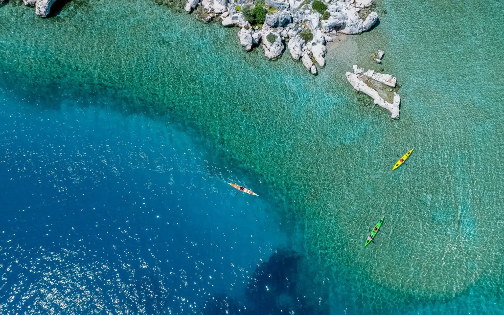 People kayaking by the lush green cliffs and rocky coast of Kekova